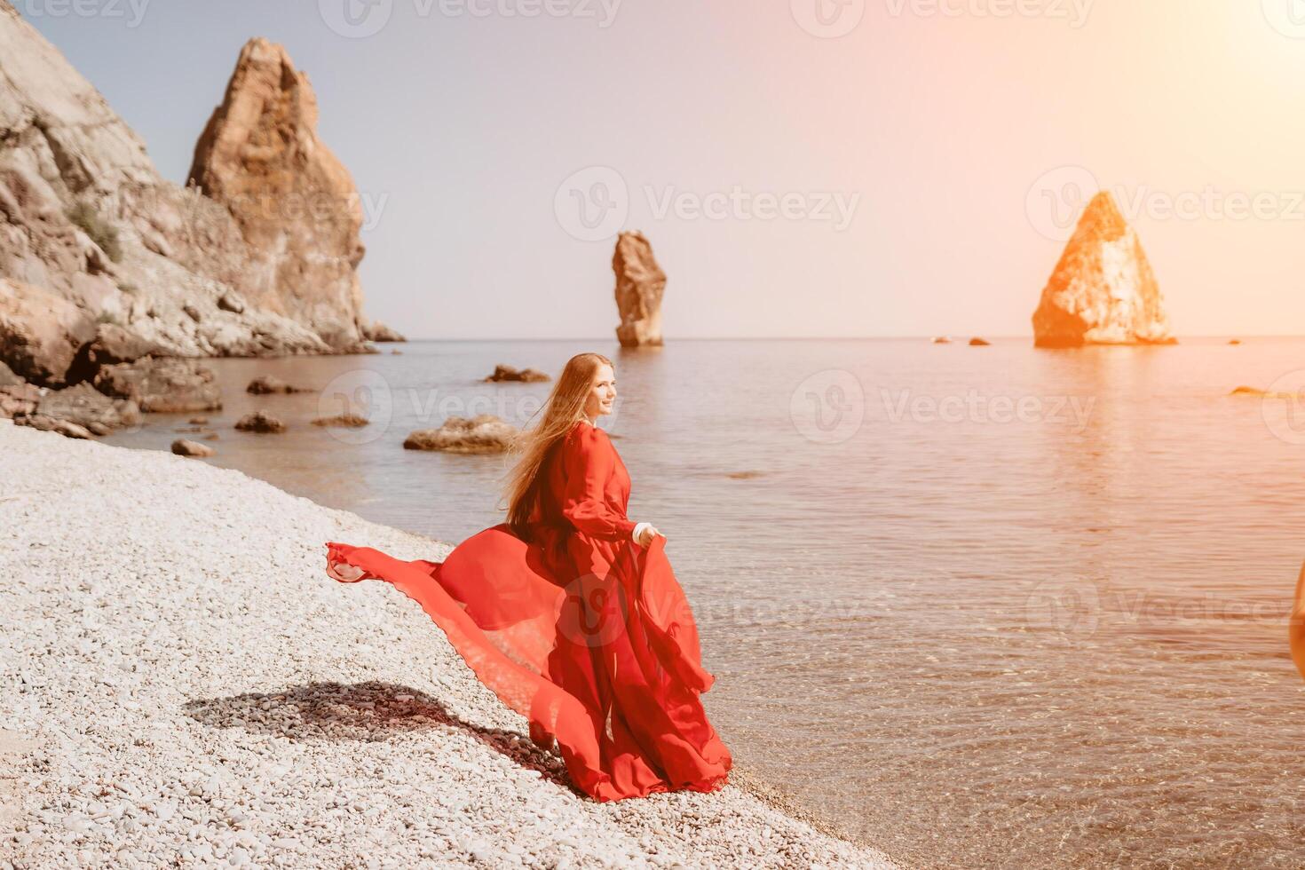 Frau Reise Meer. glücklich Tourist im rot Kleid genießen nehmen Bild draußen zum Erinnerungen. Frau Reisender posieren auf das Felsen beim Meer Bucht umgeben durch vulkanisch Berge, Teilen Reise Abenteuer Reise foto