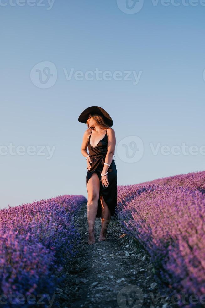 Frau Lavendel Feld. glücklich sorglos Frau im schwarz Kleid und Hut mit groß Rand Gehen im ein Lavendel Feld während Sonnenuntergang. perfekt zum inspirierend und warm Konzepte im Reise und Fernweh. foto