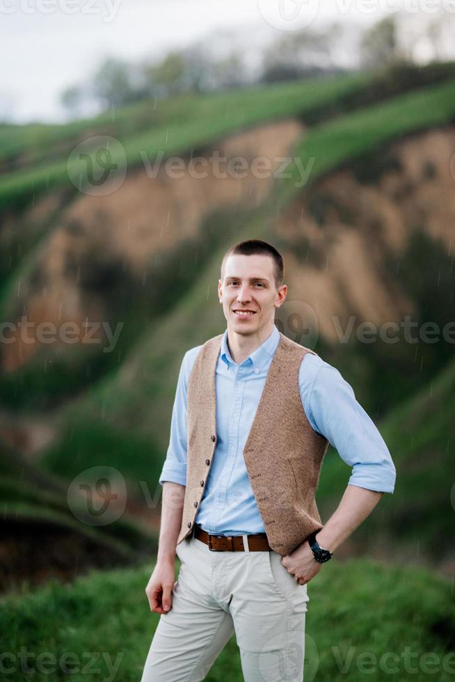 ein junger mann in einem braunen anzug vor dem hintergrund grüner berghänge foto