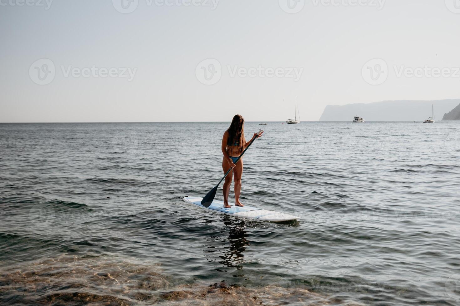 Frau Meer sup. schließen oben Porträt von glücklich jung kaukasisch Frau mit lange Haar suchen beim Kamera und lächelnd. süß Frau Porträt im ein Blau Bikini posieren auf sup Tafel im das Meer foto