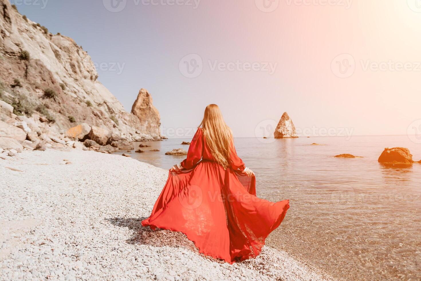 Frau Reise Meer. glücklich Tourist im rot Kleid genießen nehmen Bild draußen zum Erinnerungen. Frau Reisender posieren auf das Felsen beim Meer Bucht umgeben durch vulkanisch Berge, Teilen Reise Abenteuer Reise foto