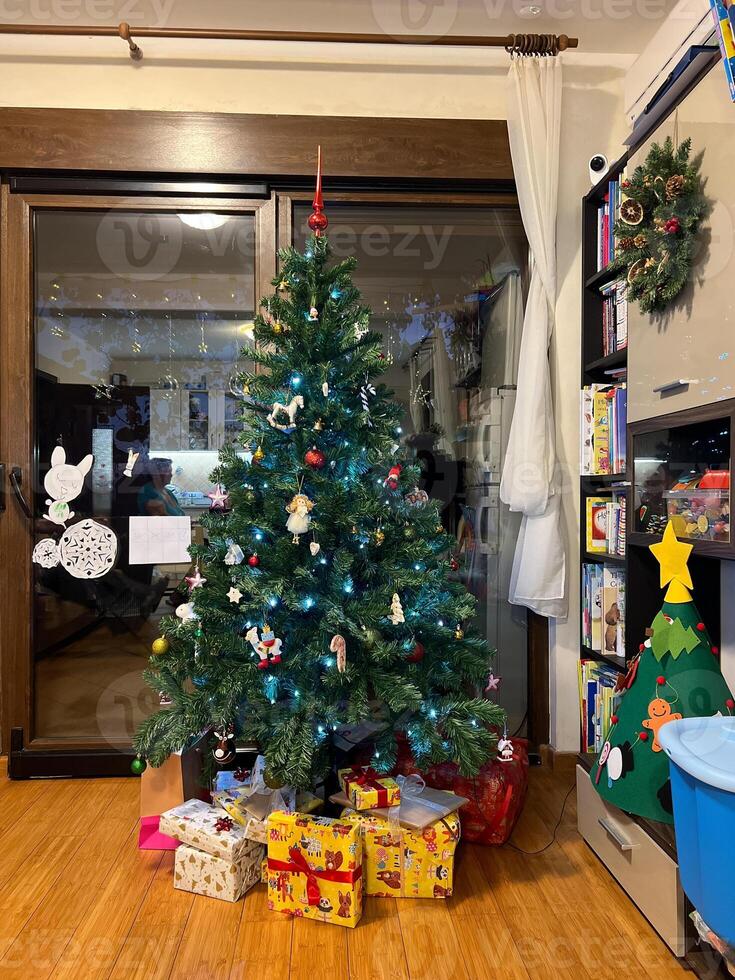 mehrfarbig Kisten mit Geschenke Lüge in der Nähe von das dekoriert Weihnachten Baum im das Zimmer foto