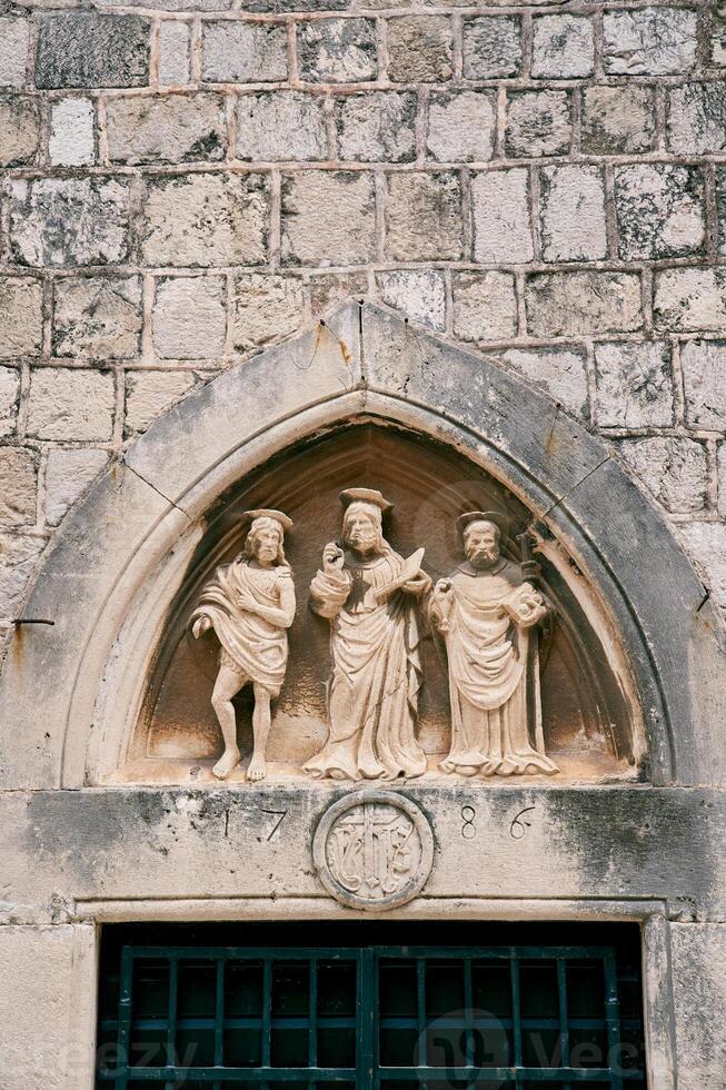 Statuen von drei Heilige im ein Lünette über das Vorderseite Tür von das Kirche von st. Lukas. Dubrovnik, Kroatien foto