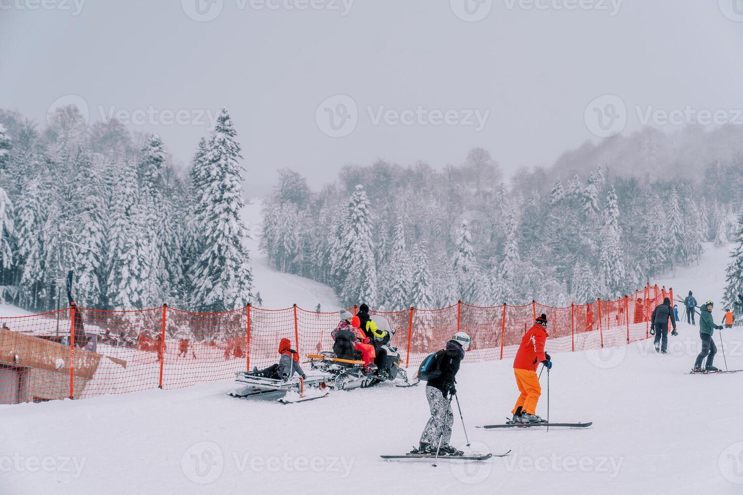Schneemobil mit ein Schlitten Fahrten Vergangenheit Skifahrer auf ein schneebedeckt Berg entlang ein rot Zaun foto