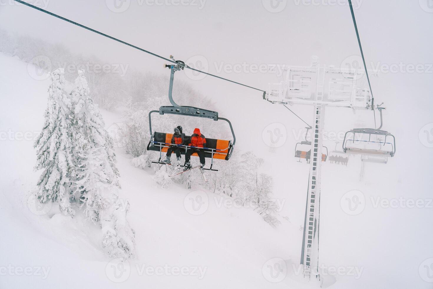 Touristen Reiten auf ein Ski Aufzug auf ein nebelig Berg über schneebedeckt Bäume foto