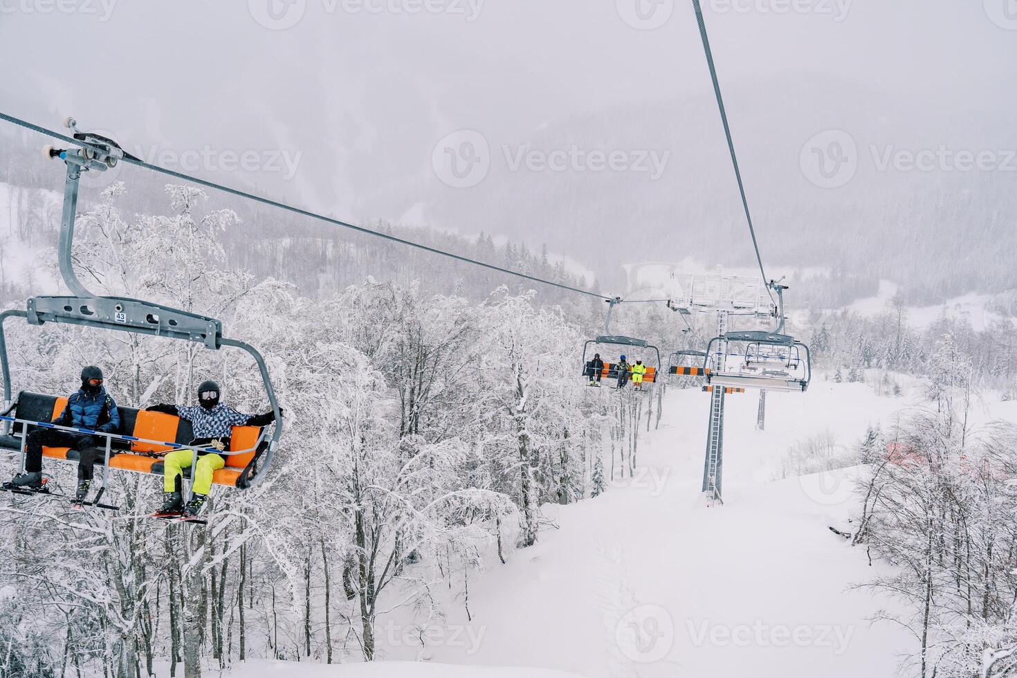 Skifahrer Reiten ein Viersitzer Sessellift Über ein schneebedeckt Wald oben das Berg foto