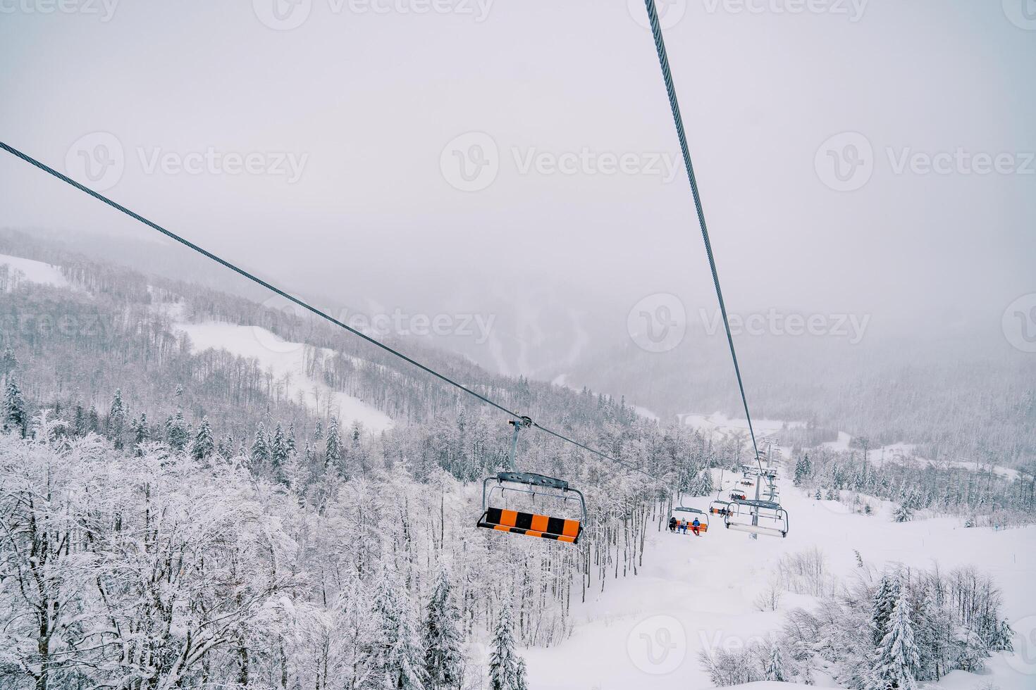 Sechssitzer Sessellift bewegt sich bergauf über ein schneebedeckt Wald foto