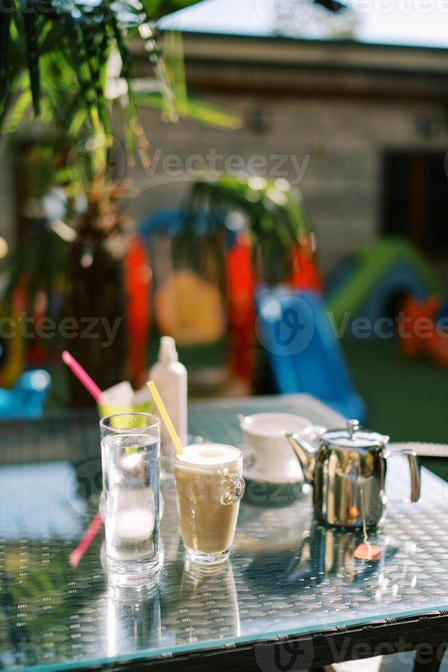 Cappuccino mit ein Stroh steht im ein Glas auf das Tabelle Nächster zu ein Milch Krug und ein Tasse von Kaffee foto