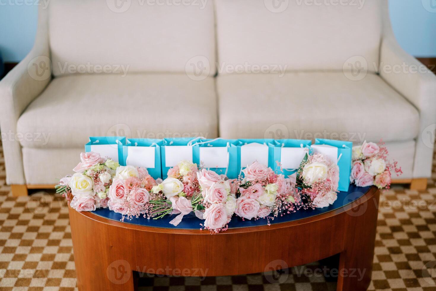 klein Blumensträuße von Rosa Rosen Lüge auf das Tabelle in der Nähe von Blau Geschenk Taschen im das Zimmer foto