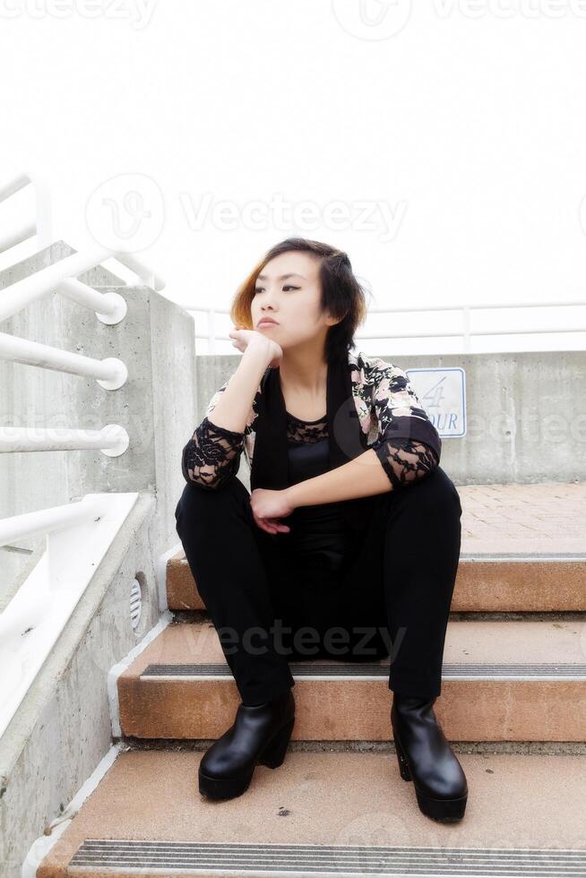 dünn asiatisch amerikanisch Frau Sitzung auf draußen Treppe foto