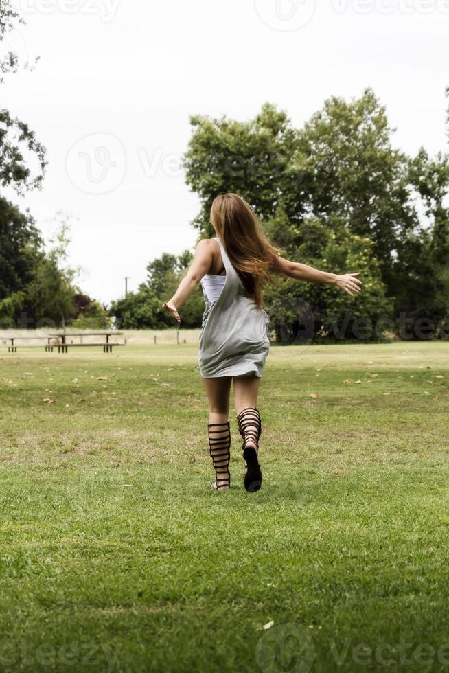 Teen Mädchen im grau Kleid und Sandalen Laufen auf Gras foto