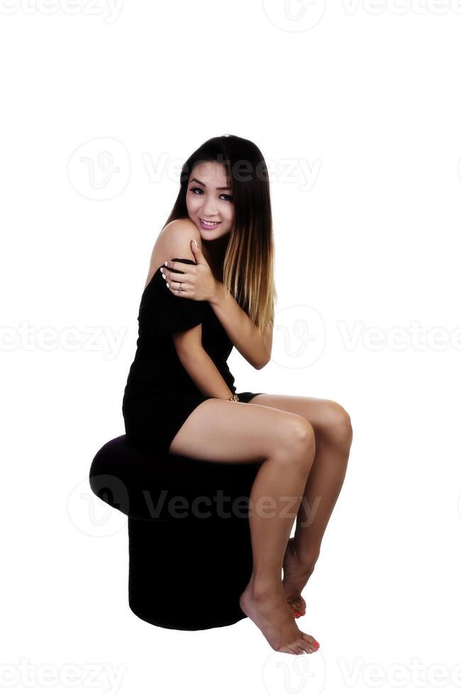 asiatisch amerikanisch Frau Sitzung auf Schemel im schwarz Kleid foto