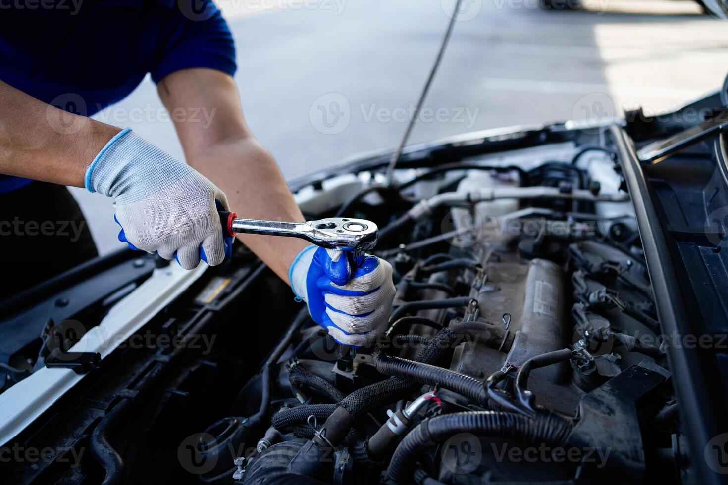 ein Mann ist Arbeiten auf ein Auto Motor. er ist tragen Blau Handschuhe und ein Blau Shirt. das Auto ist geparkt auf das Seite von das Straße foto