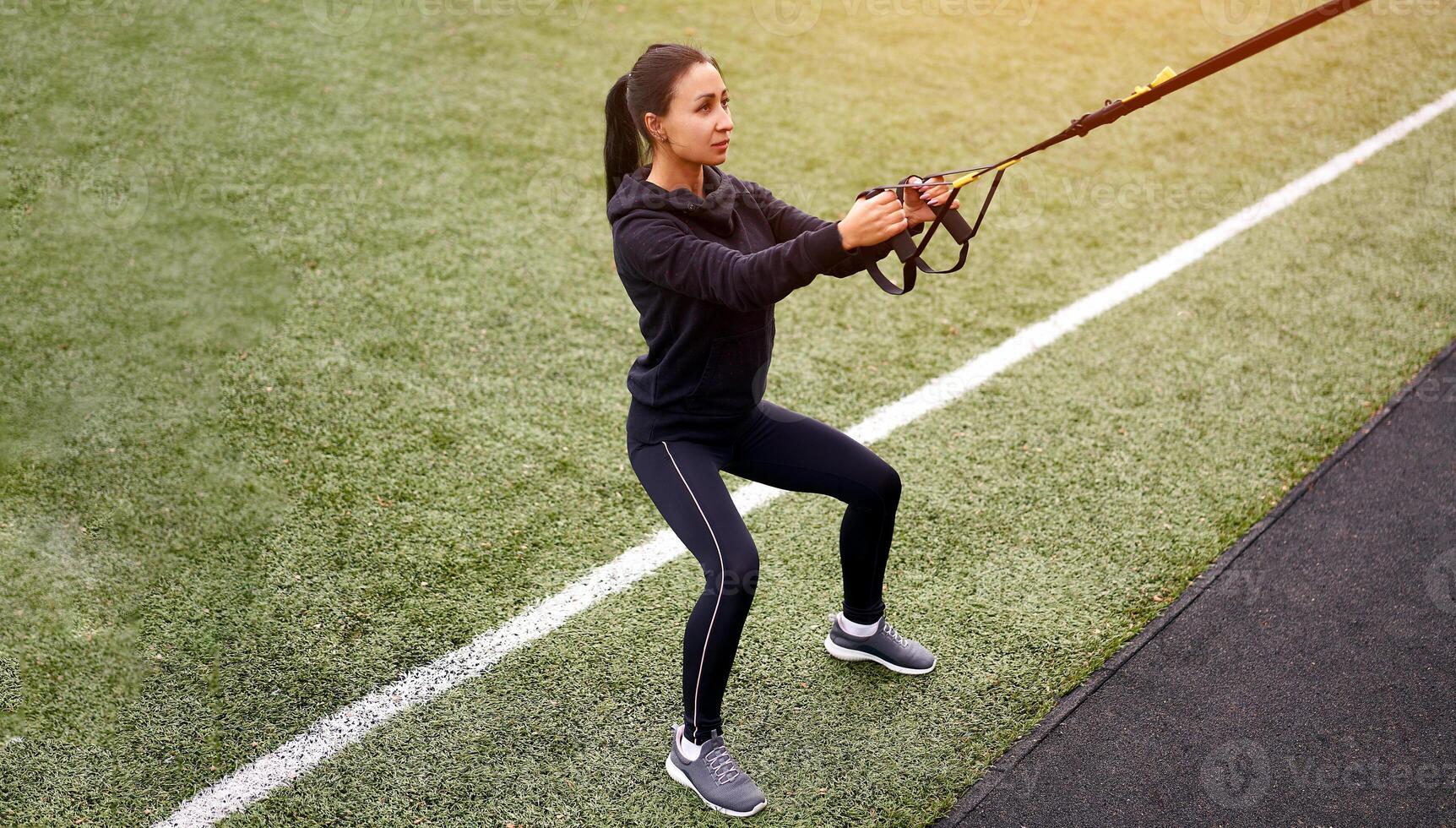 Mädchen Athlet Ausbildung mit trx auf Sportplatz. gemischt Rennen jung Erwachsene Frau tun trainieren mit Suspension System. gesund Lebensstil. Dehnen draußen Spielplatz. foto