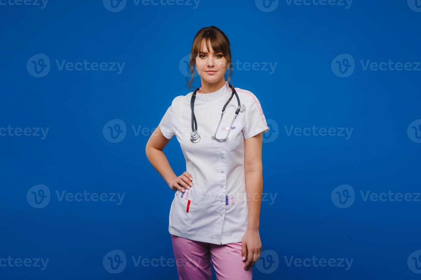 ein weiblich Arzt, gestikulierend, prüft das Herzschlag im das Arzt Büro beim das Krankenhaus mit ein Stethoskop isoliert auf ein Blau Hintergrund foto