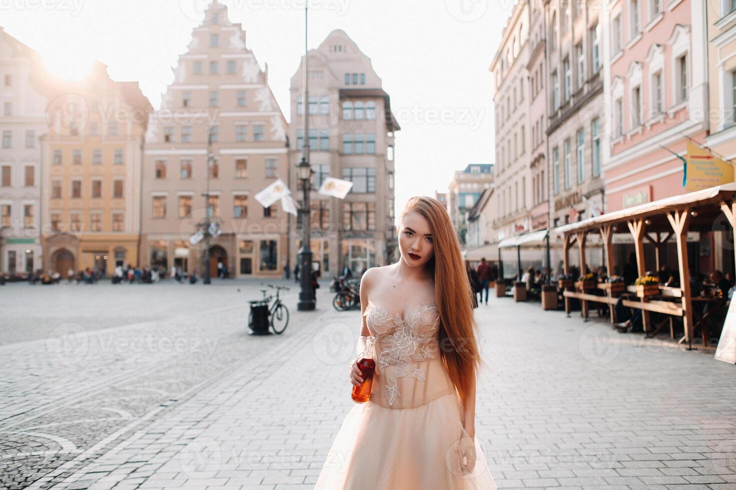 ein Braut im ein Hochzeit Kleid mit lange Haar und ein trinken Flasche im das alt Stadt, Dorf von Breslau. Hochzeit Foto schießen im das Center von ein alt Polieren Stadt Breslau, Polen