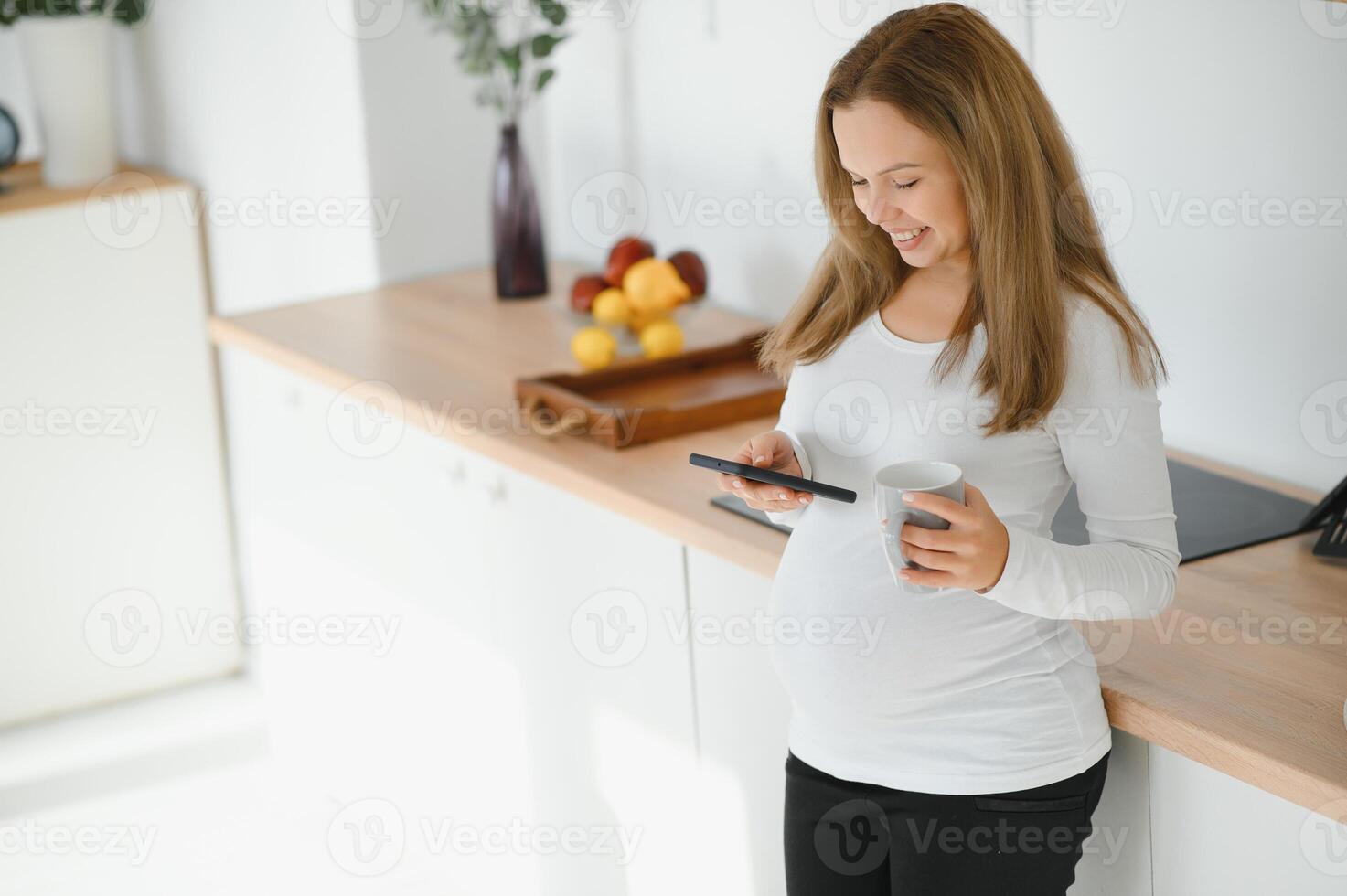 damit nett zu hören Sie schön jung schwanger Frau reden auf Telefon und suchen Weg mit Lächeln während Stehen beim Küche Innere foto