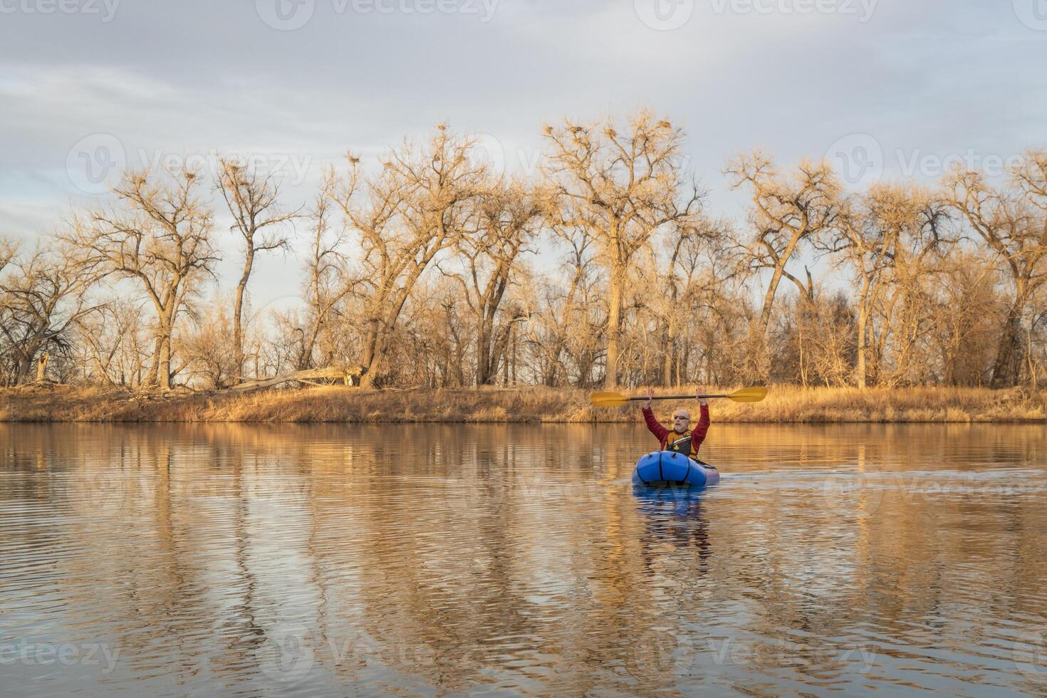 Senior männlich ist Paddeln ein aufblasbar Packraft auf ein Ruhe See mit Reiher Kolonie im früh Frühling im Nord Colorado foto