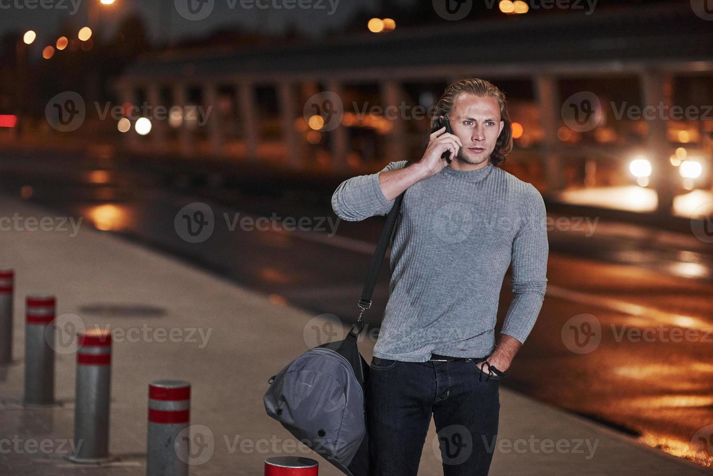 sich Sorgen machen. Mann mit langen Haaren und Reisegepäck wartet darauf, dass das Taxi ihn abholt foto