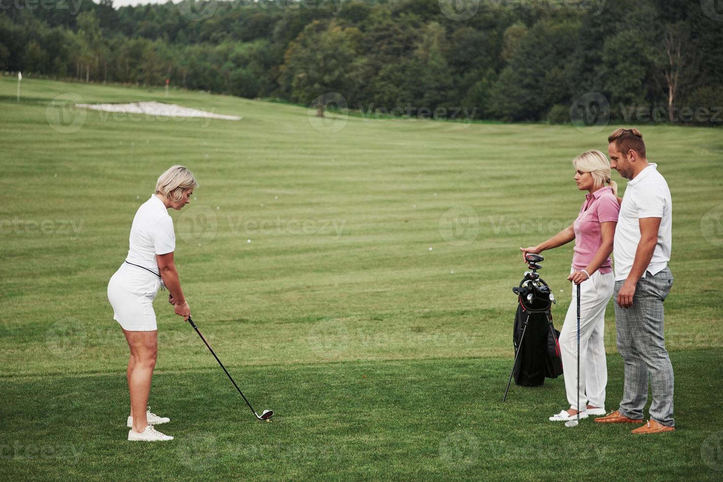 Gruppe stilvoller Freunde auf dem Golfplatz lernen ein neues Spiel zu spielen foto