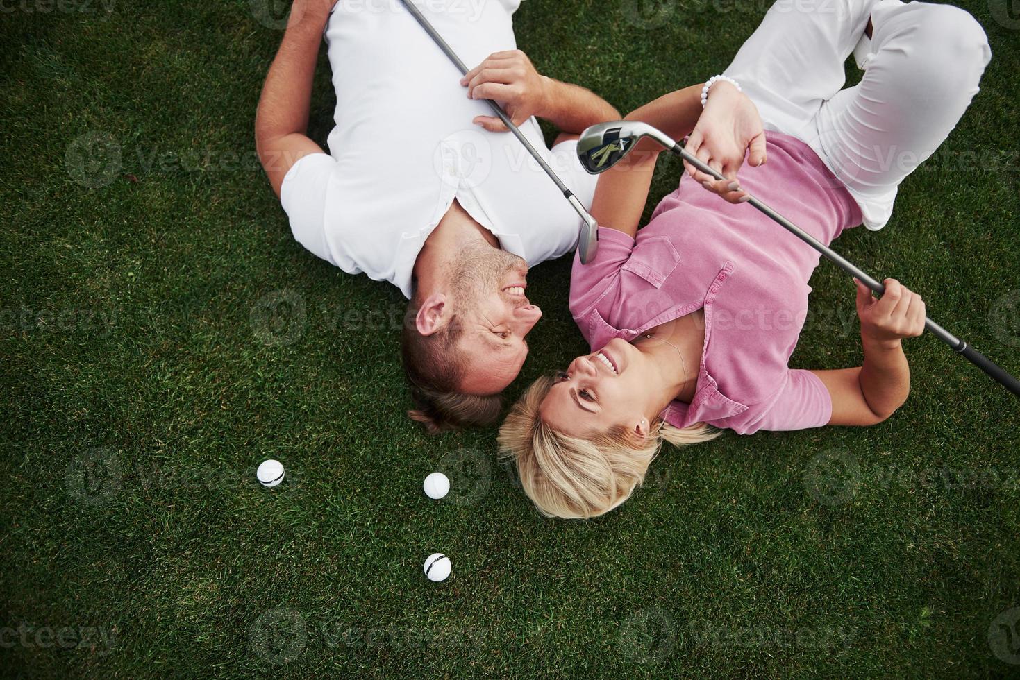 ein paar, mann und frau liegen auf dem golfplatz und entspannen nach dem spiel foto