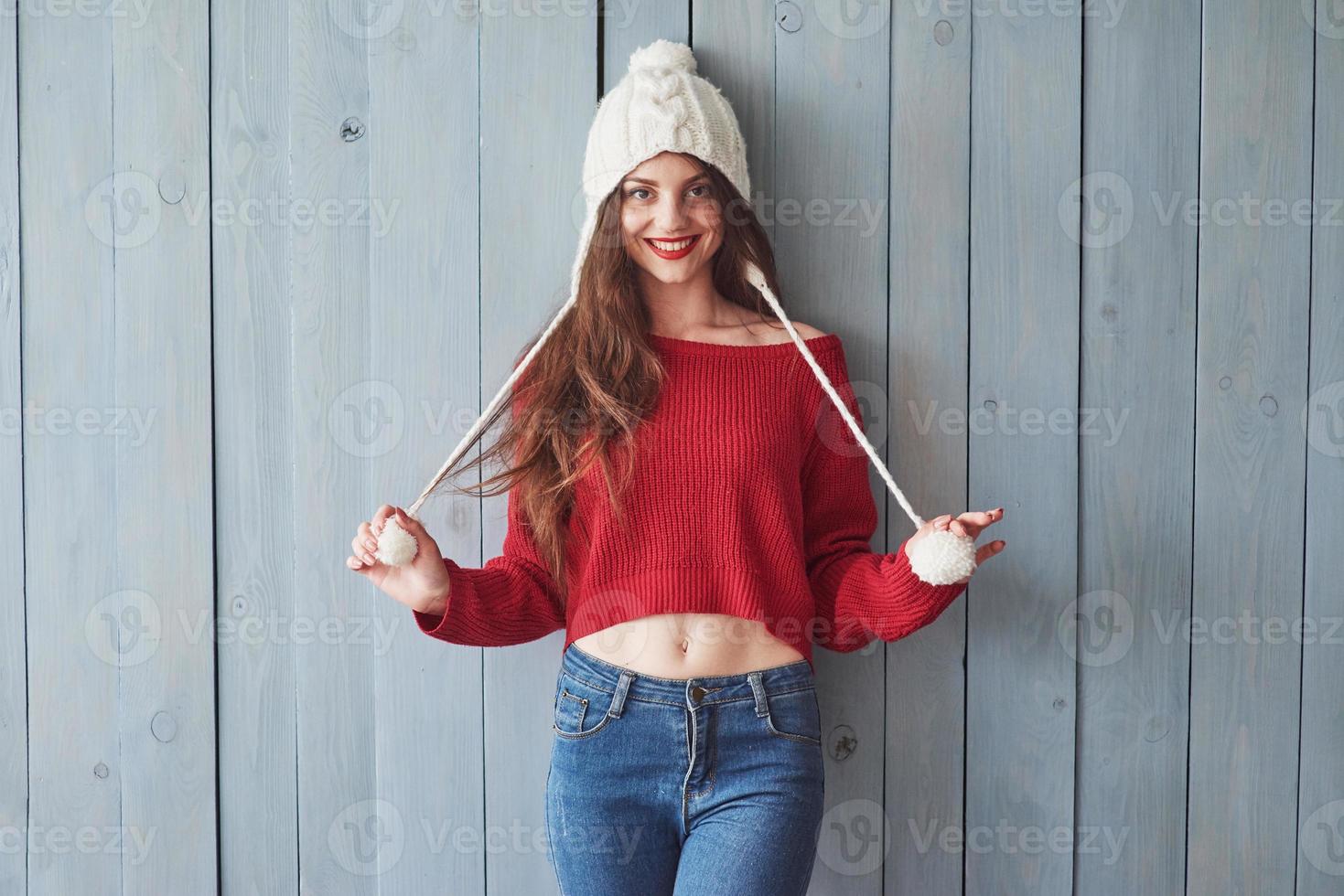 lustiges Mädchen in Strickpullover und Mütze, das drinnen mit Holzhintergrund steht foto