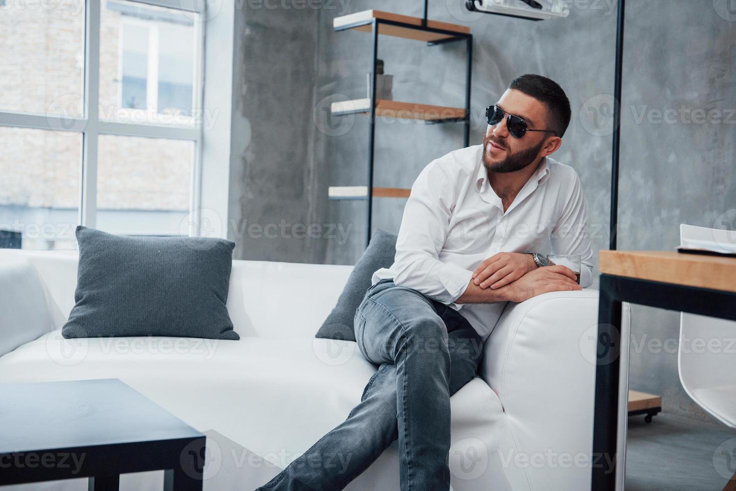 junger kurzhaariger Mann mit Sonnenbrille sitzt auf der Couch im Büro foto