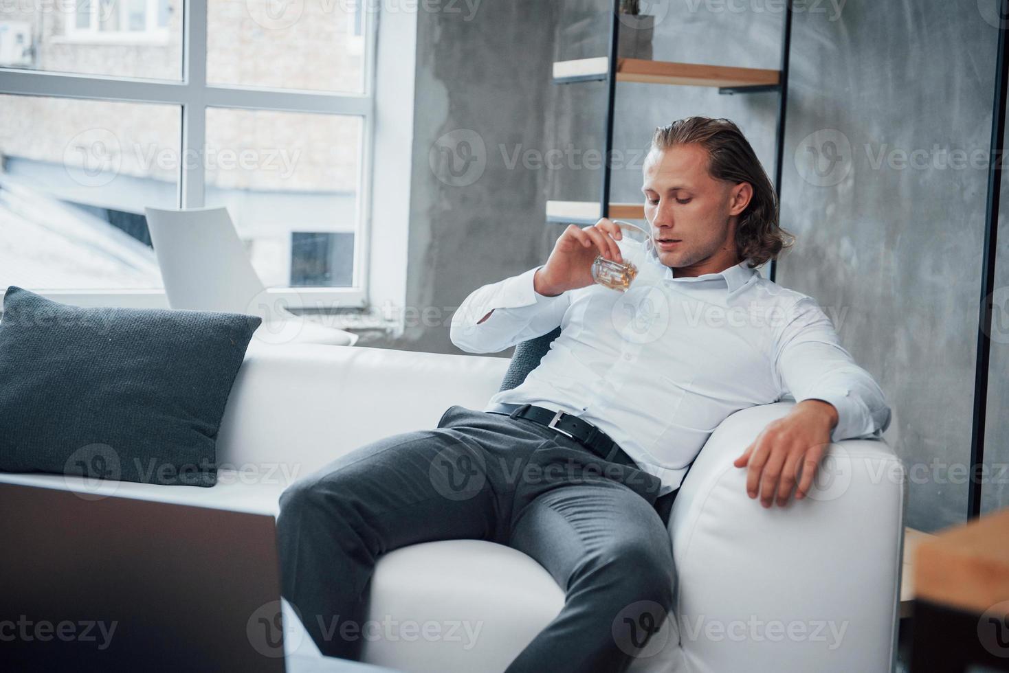 junger Mann sitzt vor einem Notebook und trinkt Whisky foto