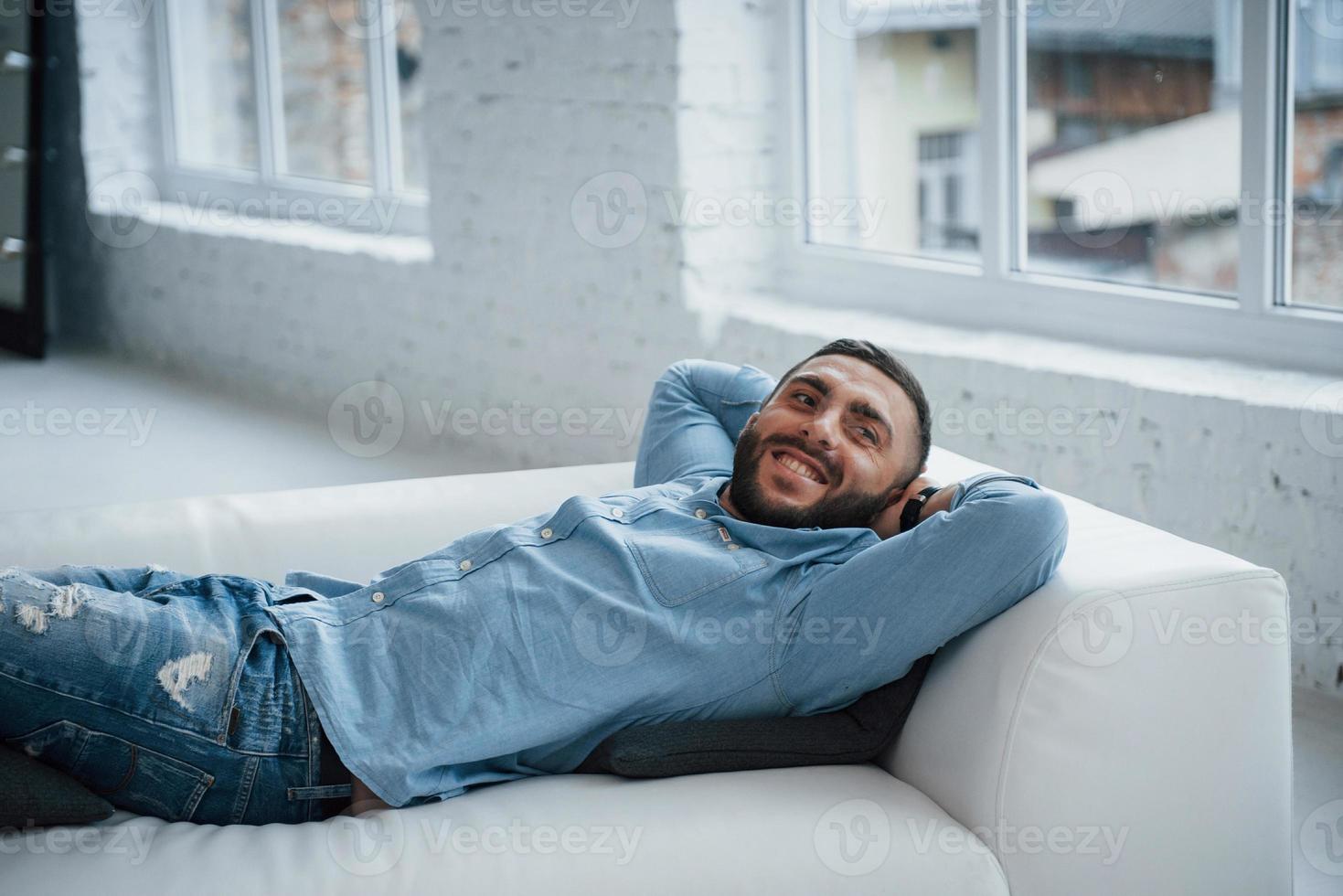 junger Mann mit Bart lächelnd und hat sich ausruhen, während er auf dem Bett liegt foto