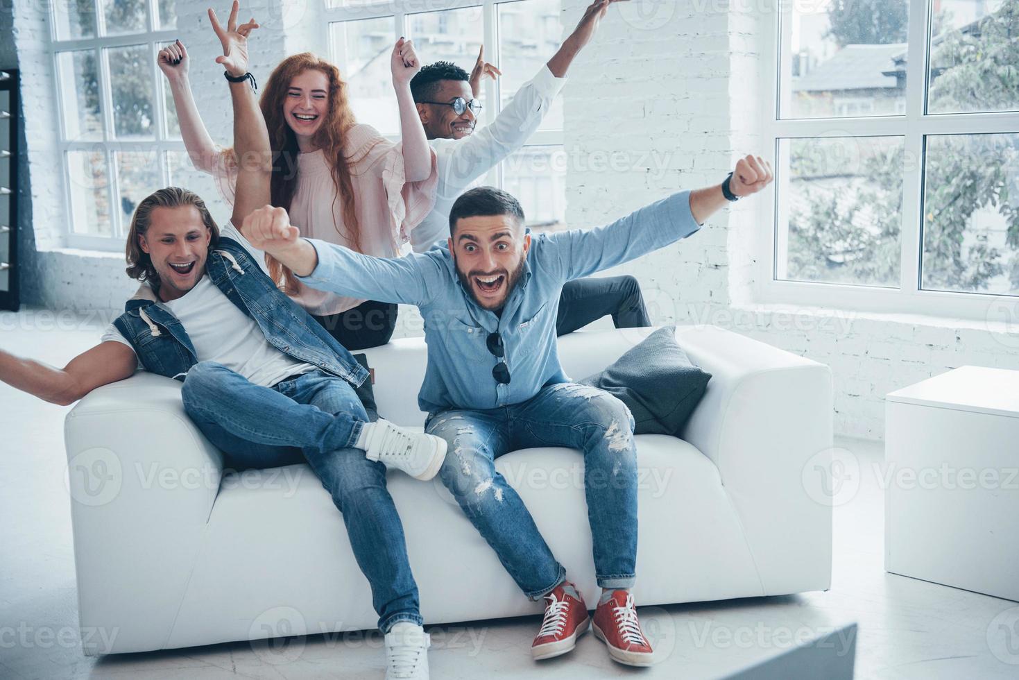 sieht aus, als hätte ihre Lieblingsfußballmannschaft gewonnen. schöne Leute sitzen auf dem Sofa mit Fenstern im Hintergrund foto