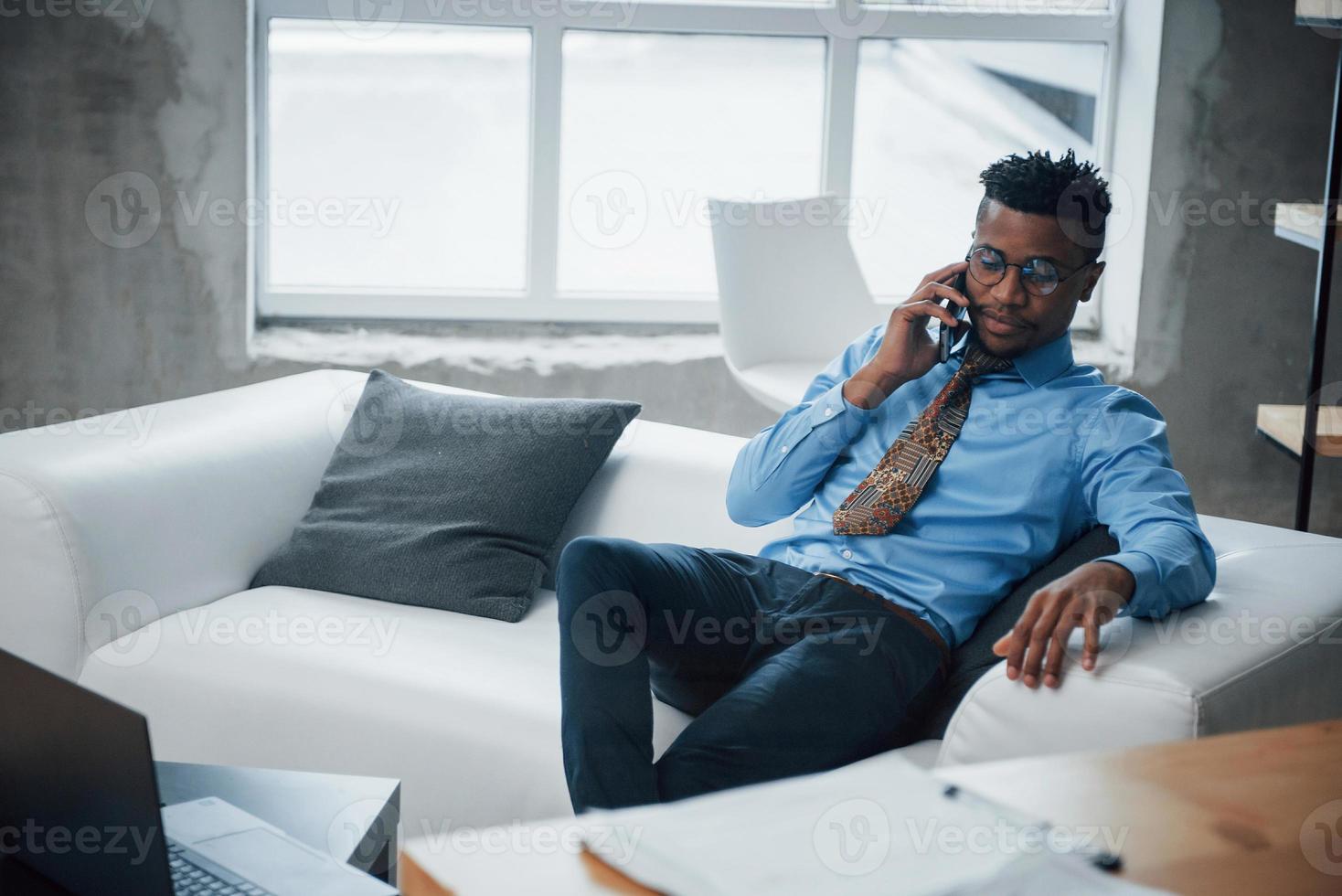 Pause. Foto von einem afroamerikanischen jungen Mann, der auf einer Couch sitzt und sich am Telefon unterhält?