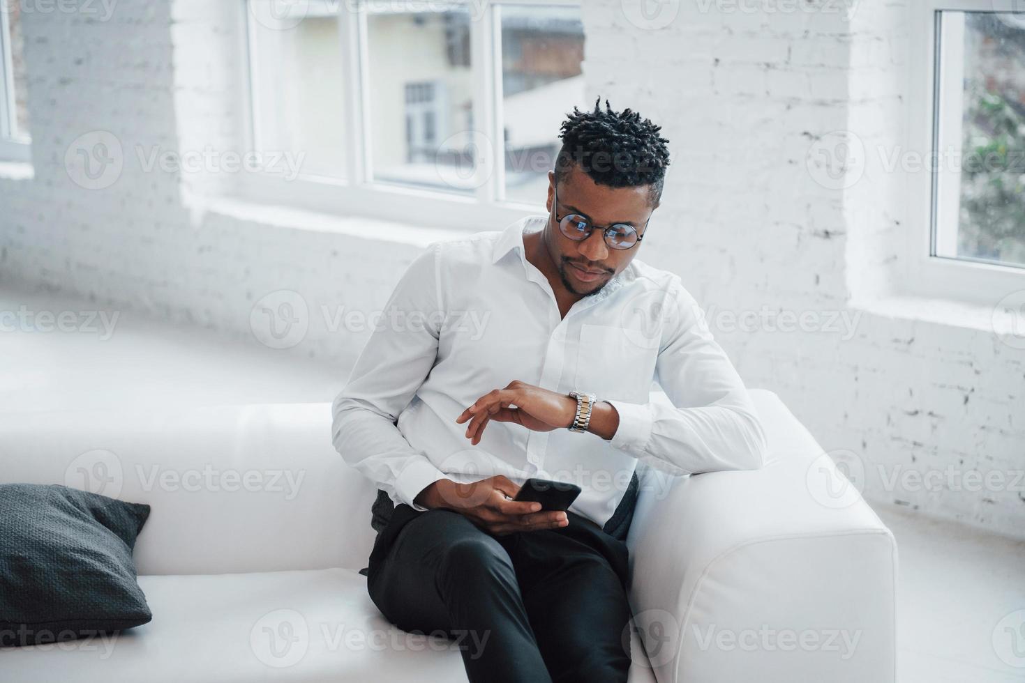 überprüfen, wie viel Zeit bis zum Ende der Pause bleibt. stylischer Afroamerikaner in klassischer Kleidung und Brille foto