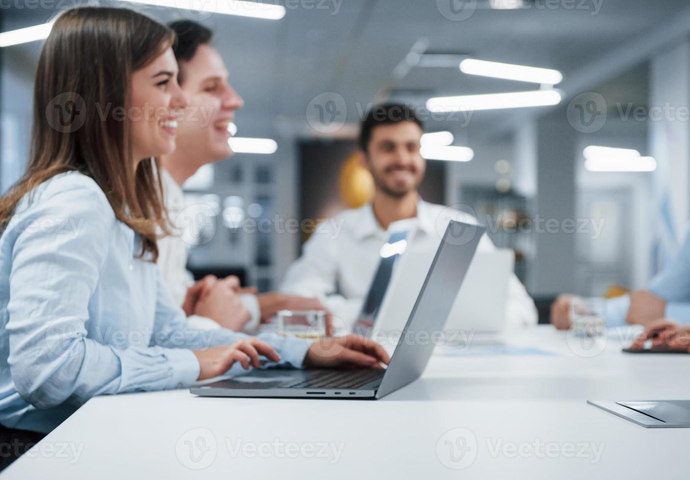Seitenansicht des Mädchens arbeitet auf dem silberfarbenen Laptop im Büro und lächelt foto
