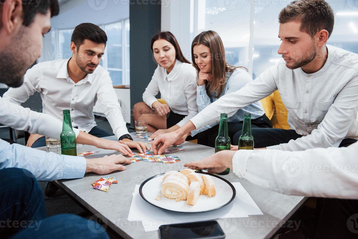 Entspannung mit Spiel. erfolgreiches Geschäft feiern. Junge Büroangestellte sitzen mit Alkohol am Tisch foto