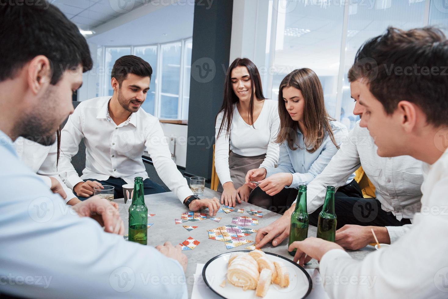 brauchen etwas mehr Konzentration. Entspannung mit Spiel. erfolgreiches Geschäft feiern. Junge Büroangestellte sitzen mit Alkohol am Tisch foto