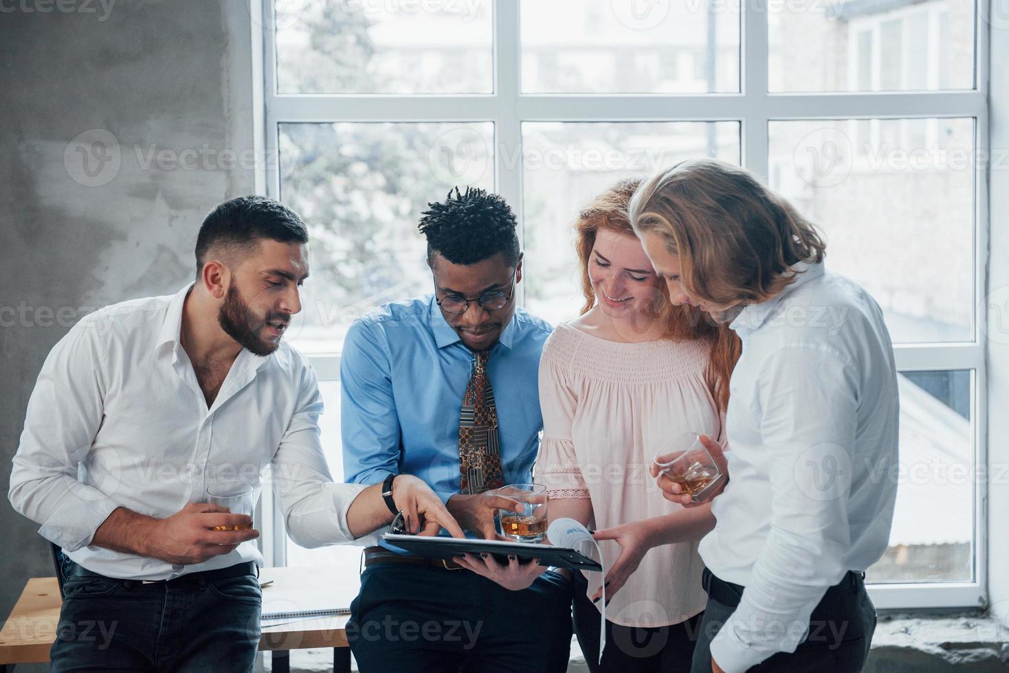 junge Geschäftsleute schauen sich Grafiken an und besinnen sich mit Whisky foto