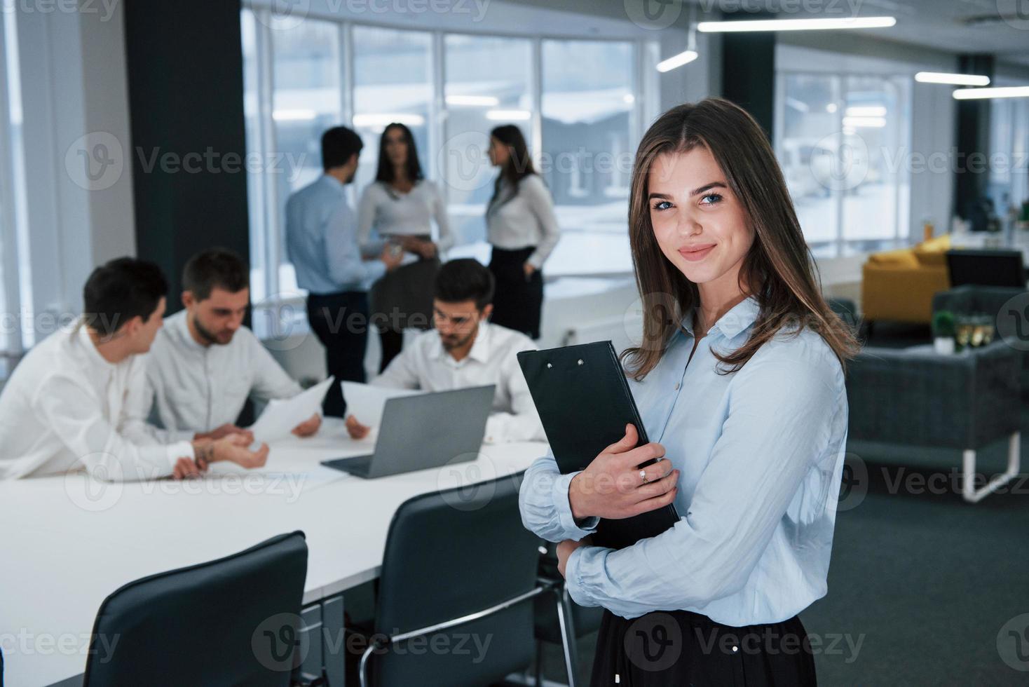 Frau bei der Arbeit. Porträt des jungen Mädchens steht im Büro mit Mitarbeitern im Hintergrund foto