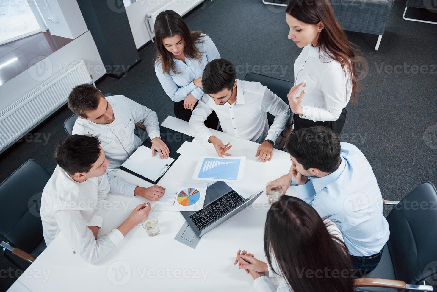 Draufsicht auf Büroangestellte in klassischer Kleidung, die mit Laptop und Dokumenten am Tisch sitzen foto