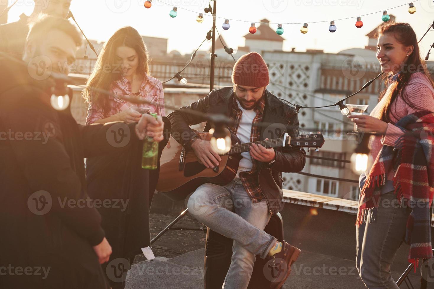 Vorderansicht. Gitarrist mit Freunden auf dem Dach am sonnigen Tag foto