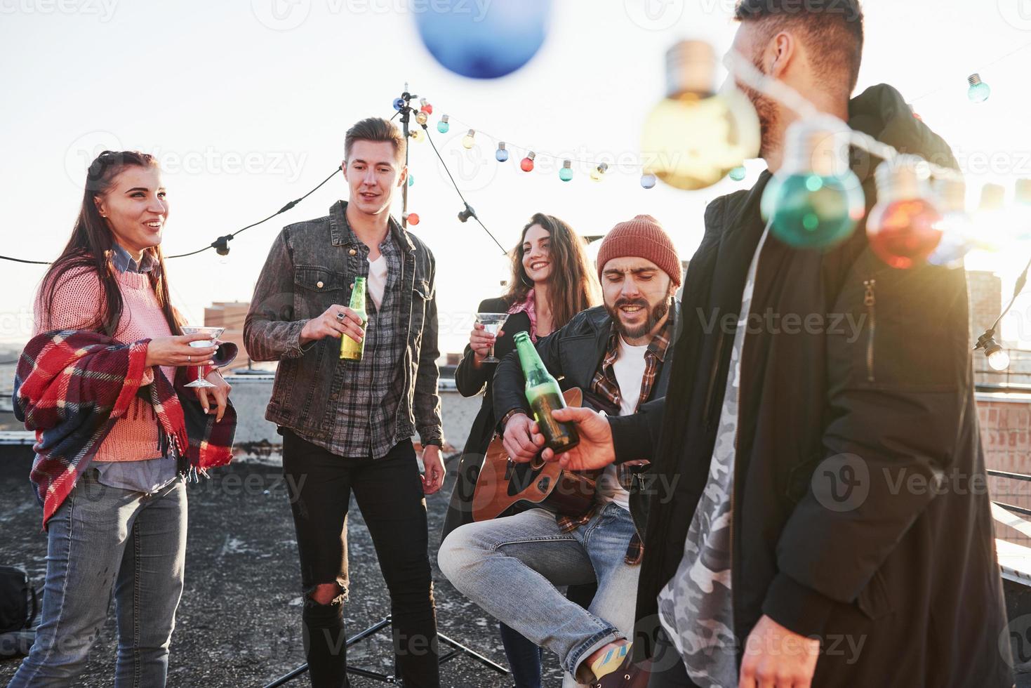 gutes Wochenende. Party auf dem Dach. Freunde mit Alkohol, die eine gute Zeit haben. Kerl, der Gitarre spielt foto