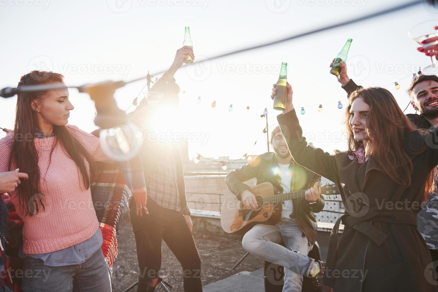 tanzen bei Sonnenschein. Gruppe junger Leute, die auf einem Dach mit etwas Alkohol und Gitarrenspiel feiern? foto