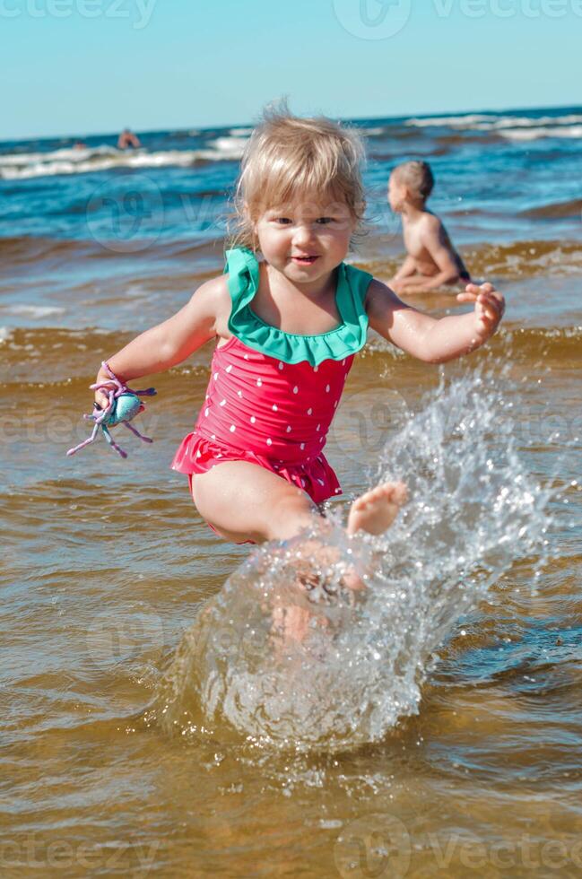 jung glücklich Kind Mädchen von europäisch Aussehen Alter von 4 haben Spaß im Wasser auf das Strand und Spritzwasser, tropisch Sommer- Berufe,Ferien.a Kind genießt das Meer.vertikal Foto. foto