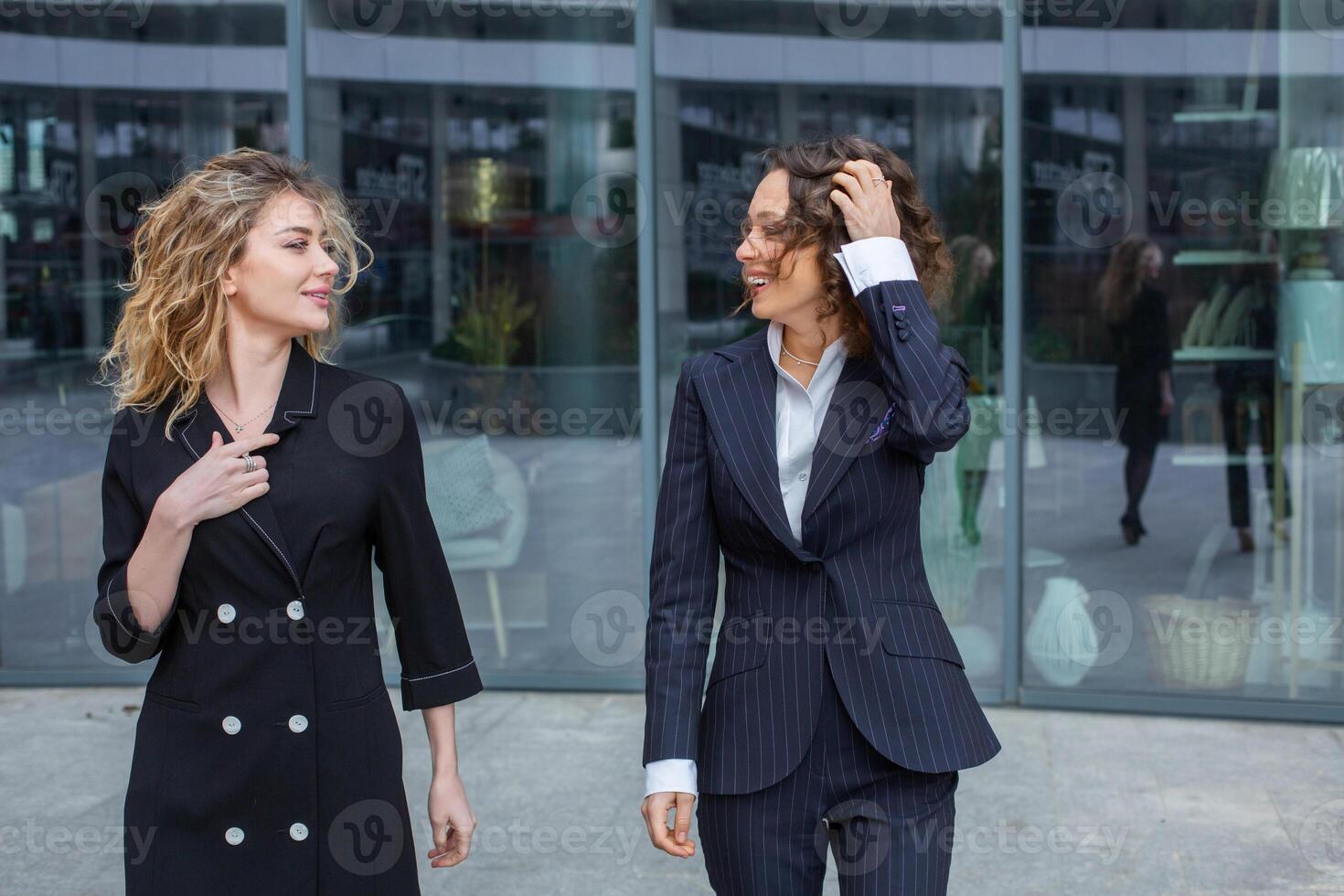 zwei erfolgreich Geschäft Frauen sind reden im das Stadt im Vorderseite von ein modern Gebäude. Geschäft Treffen auf das Straße. 2 weiblich Manager mit oben Positionen. foto