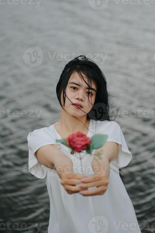 Porträt von ein ziemlich jung Frau gekleidet im Weiß Kleid halten Rose Blumen foto