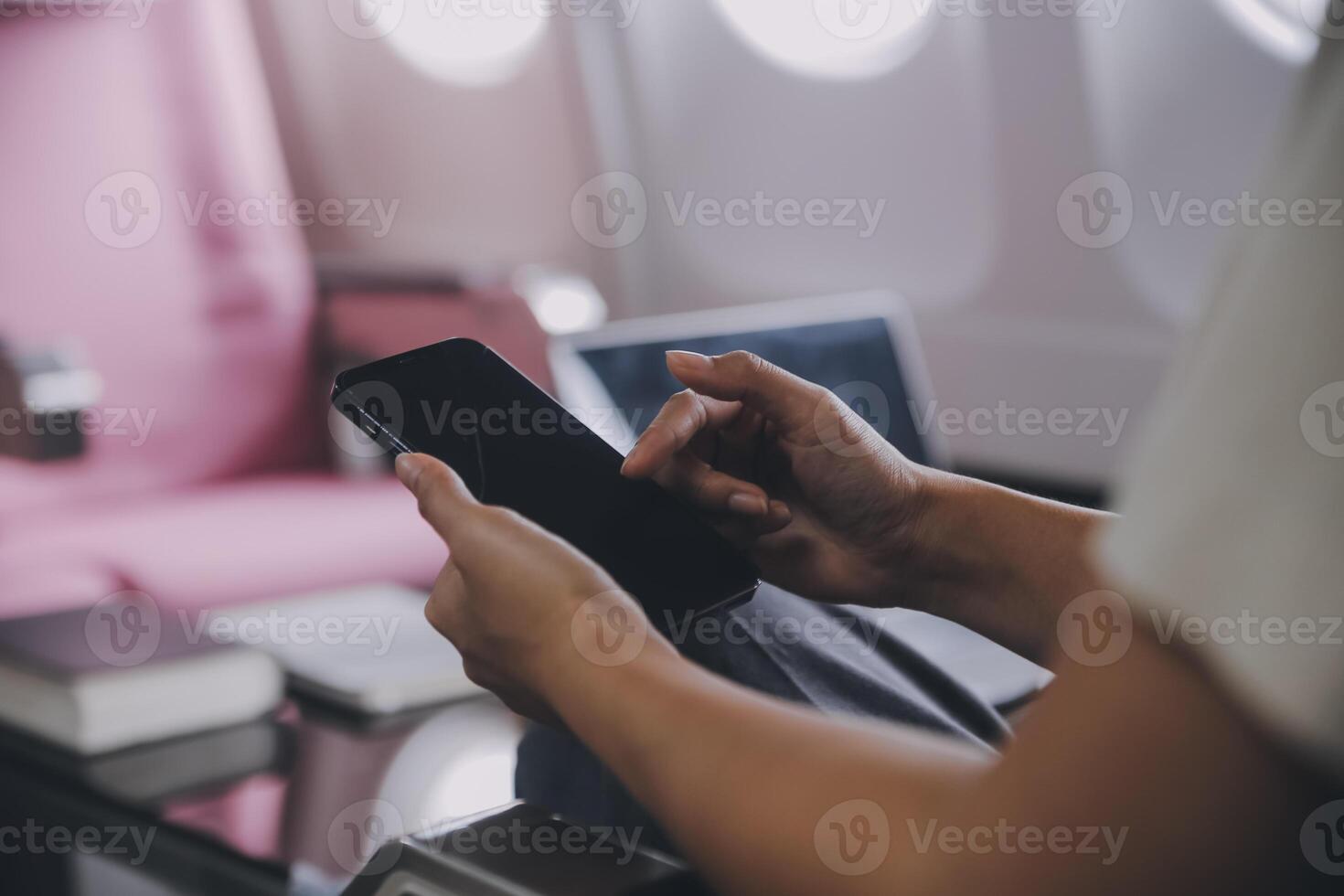 asiatische Passagierin, die im Flugzeug in der Nähe des Fensters sitzt und Nachrichten aus sozialen Netzwerken liest oder Reiseanwendungen auf dem Smartphone verwendet foto