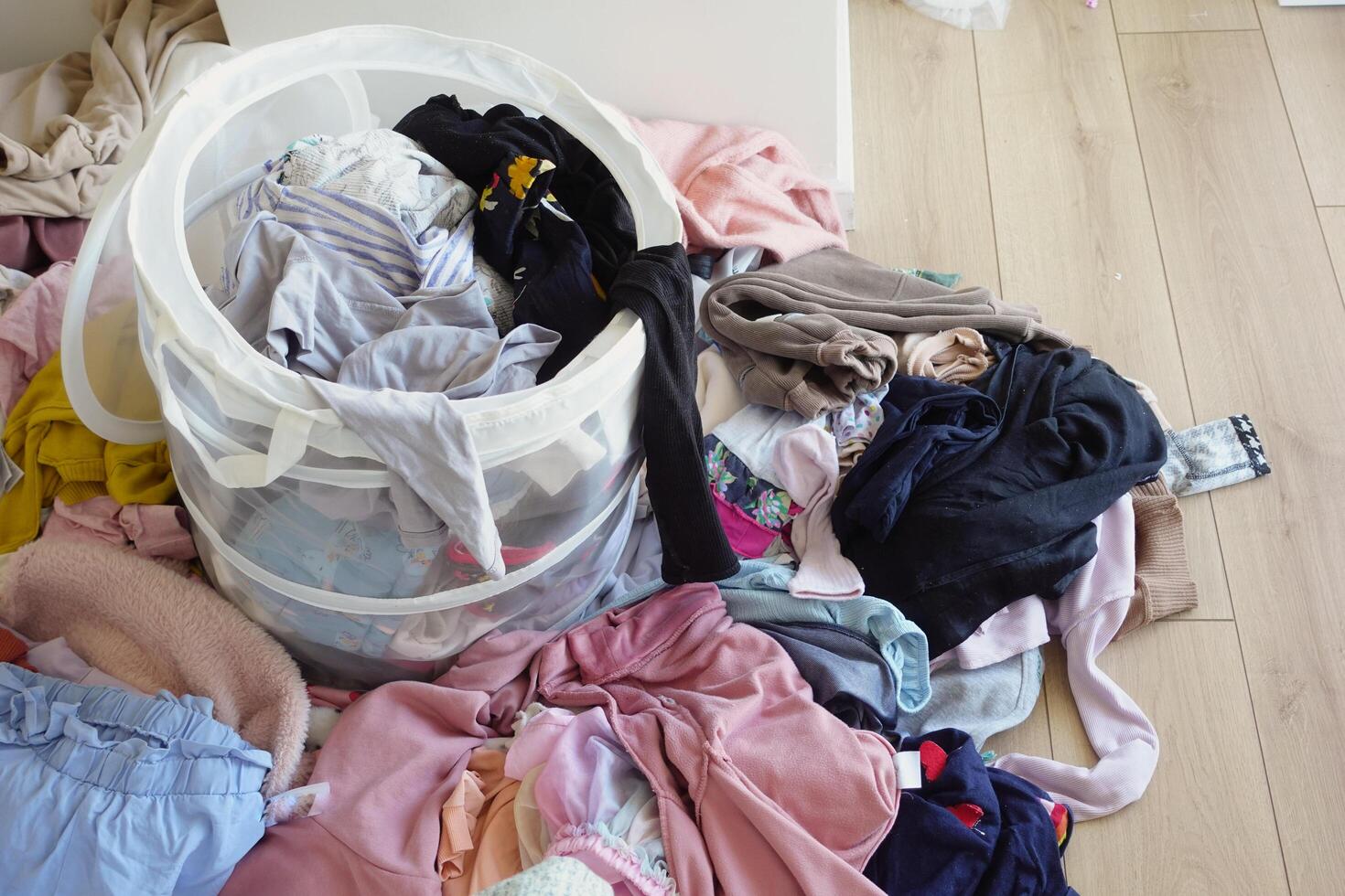 Kleider Stapel Nächster zu Wäsche Korb gefüllt mit Kleider, auf Hartholz Fußboden foto