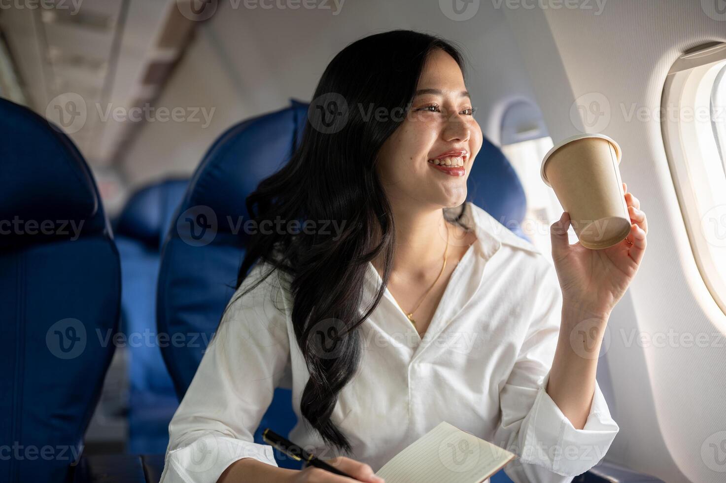 ein elegant asiatisch Geschäftsfrau ist nippen Kaffee während suchen beim das Aussicht draußen das Flugzeug Fenster. foto