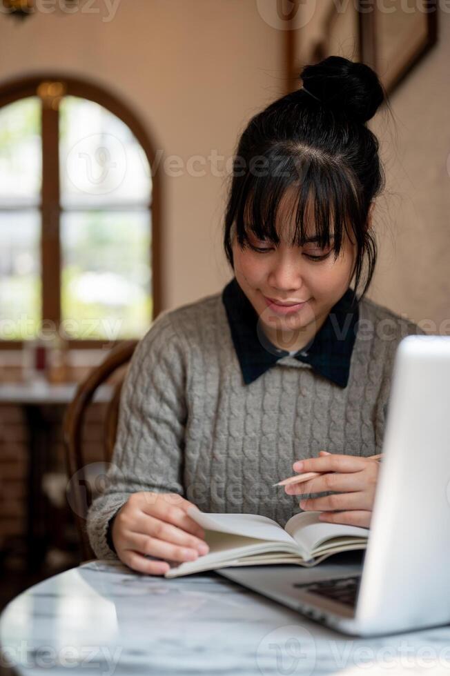 ein weiblich Universität Schüler im beiläufig tragen ist lesen ein Lehrbuch oder tun Hausaufgaben im ein Cafe. foto