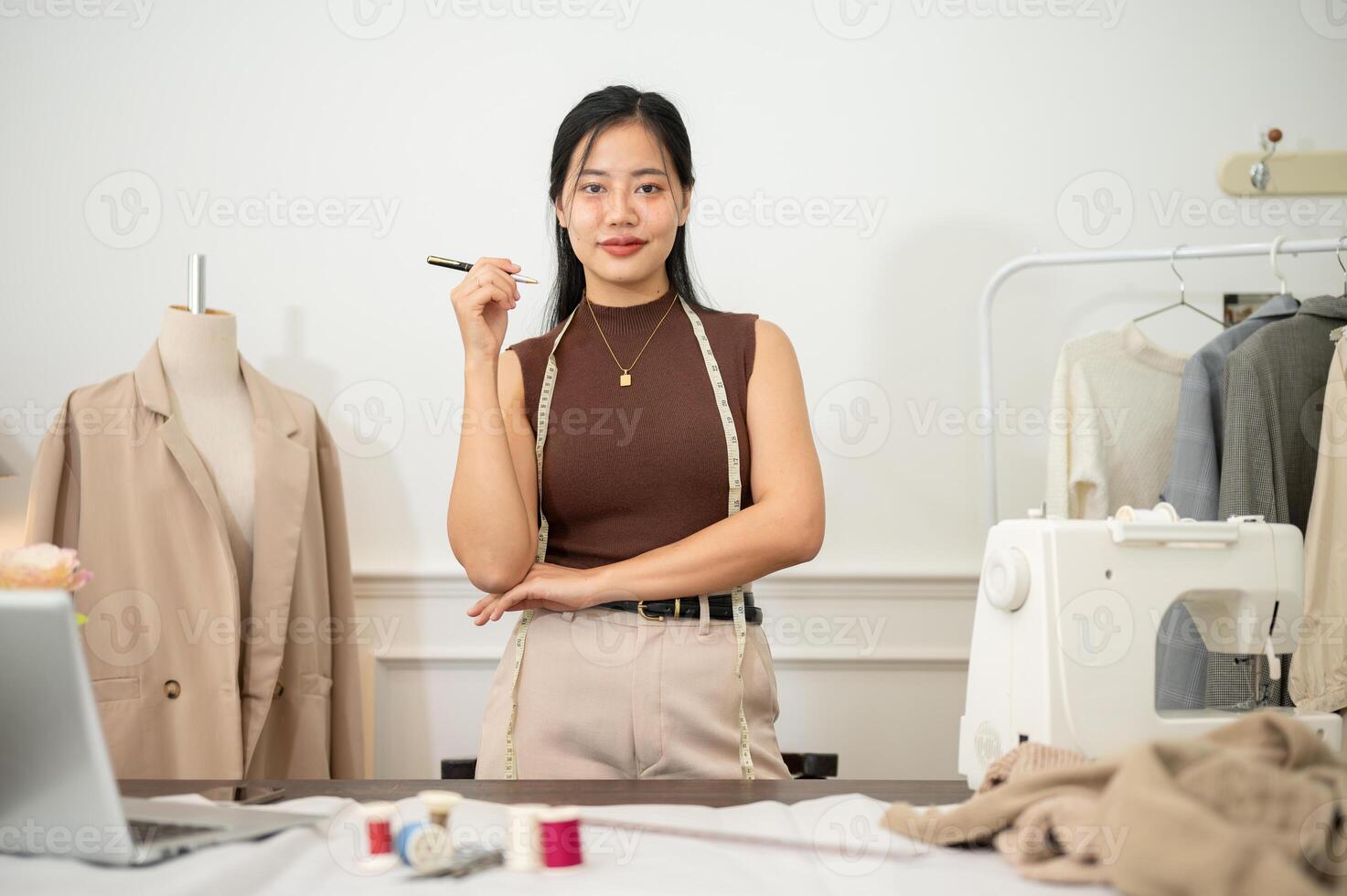 ein attraktiv asiatisch weiblich Mode Designer oder Schneider ist im ihr Studio, lächelnd beim das Kamera. foto