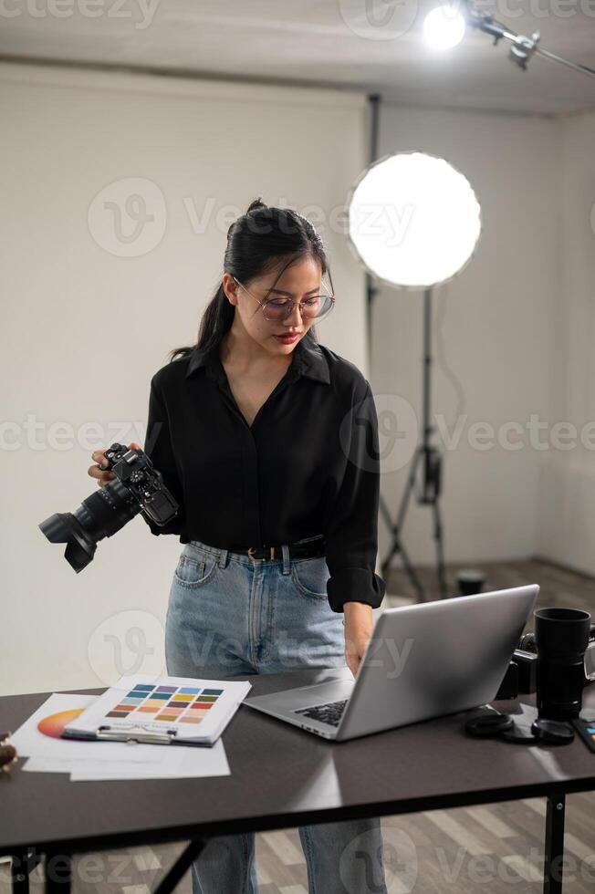 ein Fachmann asiatisch weiblich Fotograf ist Überprüfung Bilder auf ihr Laptop, Arbeiten im ein Studio. foto